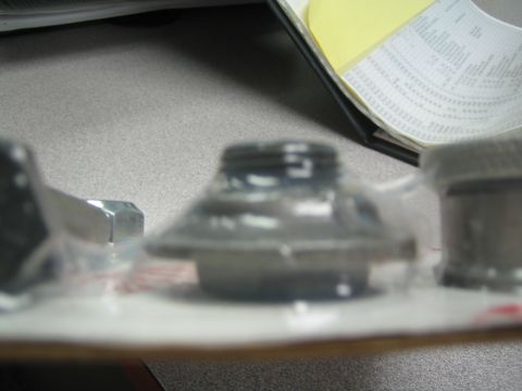 1990 Ford Bronco - blurry close-up of metal fittings and a cone-shaped part in plastic packaging beside a document on a desk.