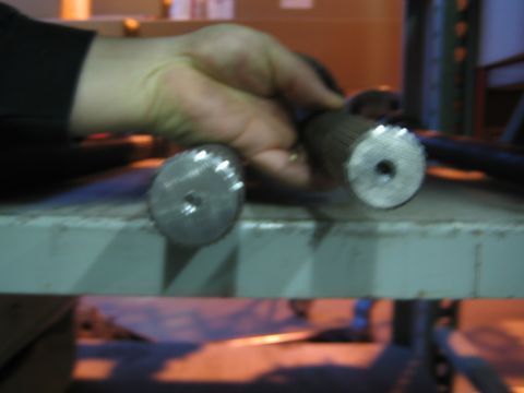 1990 Ford Bronco - hand holds two splined steel axle shafts stood on end atop a green-painted shop rack.