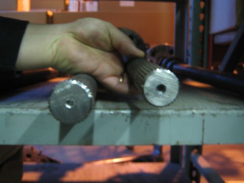 1990 Ford Bronco - hand grips two splined steel axle shaft ends resting on a green-painted metal shop rack.