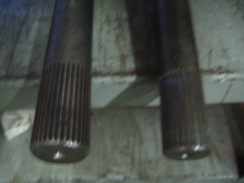 1990 Ford Bronco - Close-up of the splined ends of two steel axle shafts laid on a worn painted workbench.
