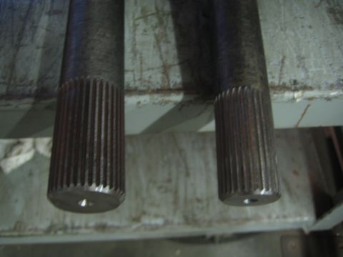 1990 Ford Bronco - Close-up of the fine-splined ends of two steel axle shafts suspended over a worn shop bench.