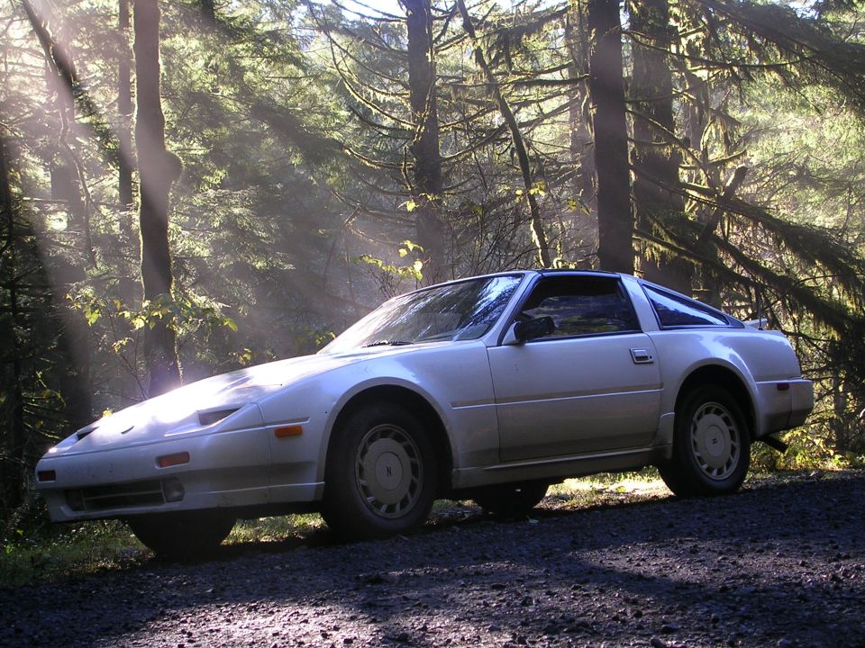 Dusty white Nissan 300ZX on gravel forest road with sunbeams through the trees