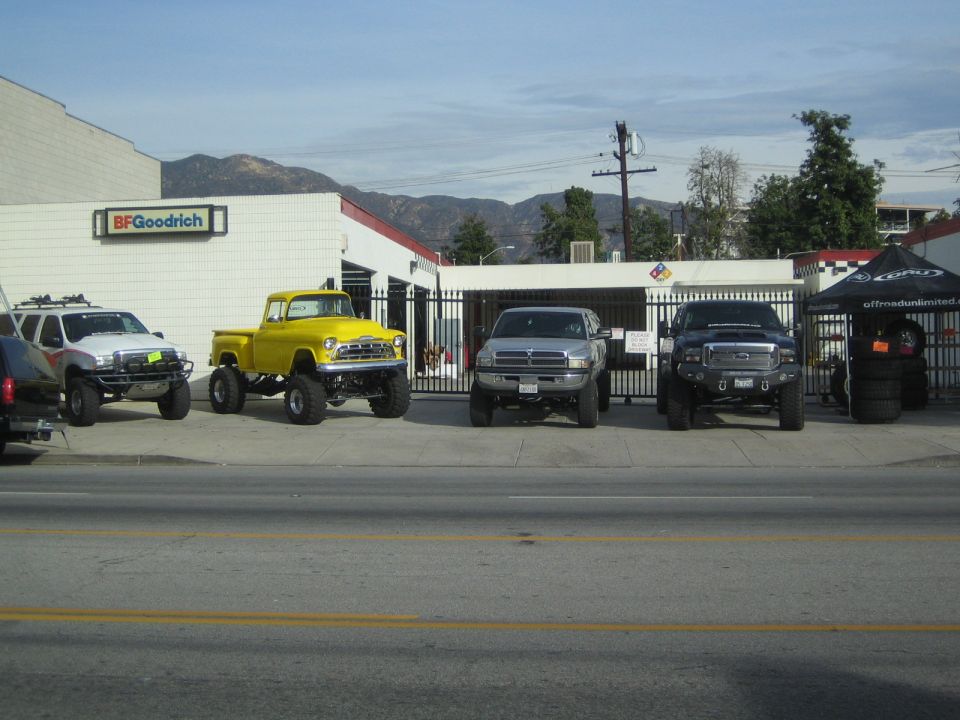 Lifted trucks parked in front of a BFGoodrich shop along a street