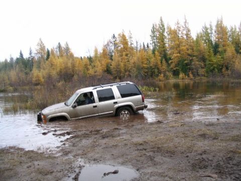 2000 Chevrolet Tahoe - A silver SUV is stuck in a muddy, watery area with trees in the background.