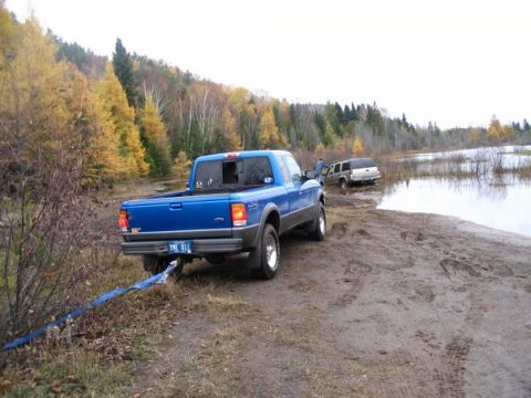 2000 Chevrolet Tahoe - Blue pickup truck is towing a white SUV out of a muddy area next to a body of water.