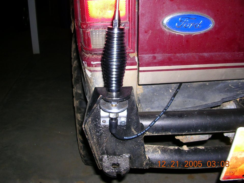 CB whip antenna on black steel bumper bracket of maroon Ford SUV, RG-8/U coax routed along bumper