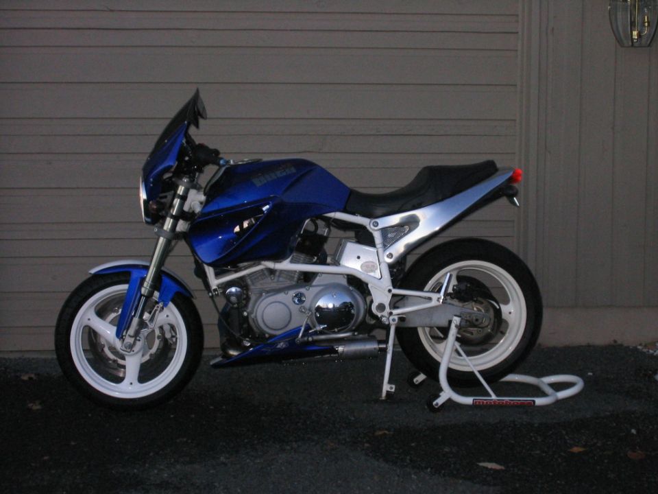 Blue Buell naked bike with white frame and wheels on a rear stand by a garage door