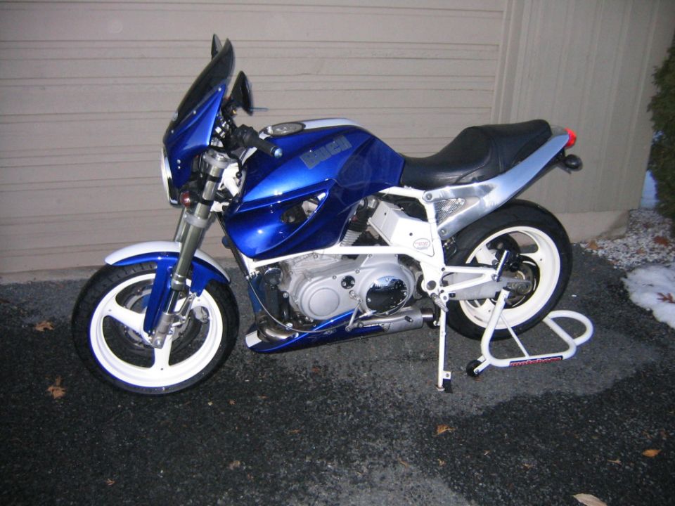 Blue Buell sportbike with white frame and wheels on a rear paddock stand by a garage