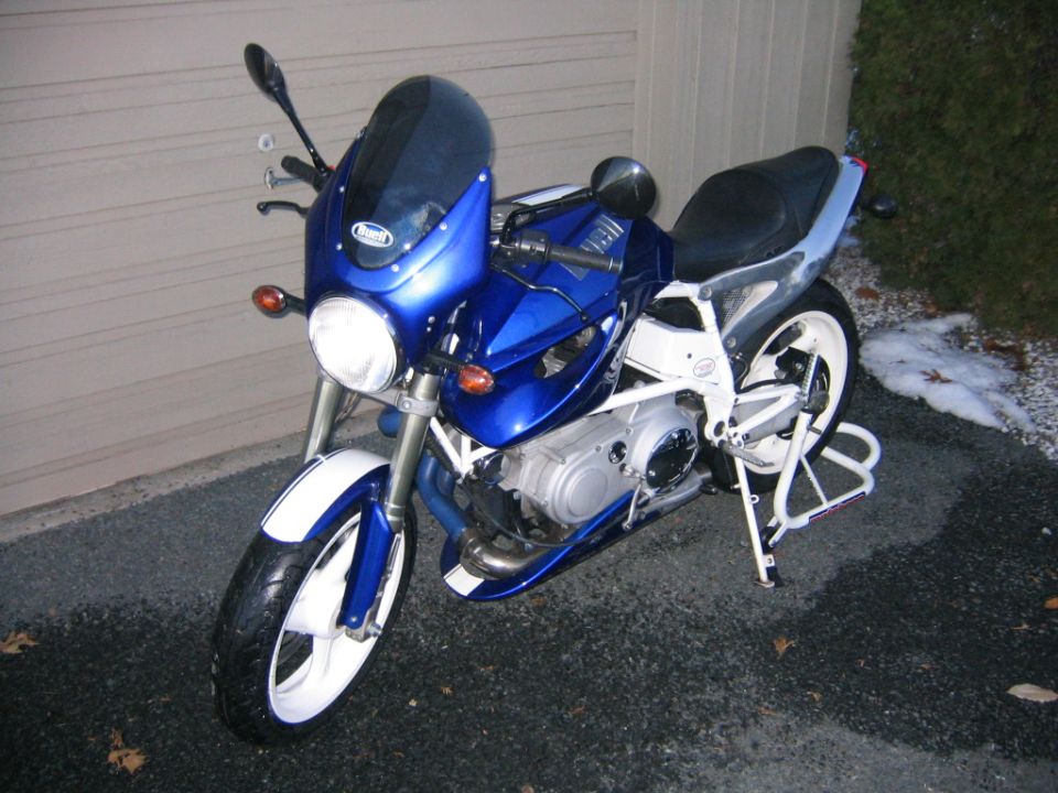 Blue Buell with white trellis frame and wheels parked on asphalt by a garage door