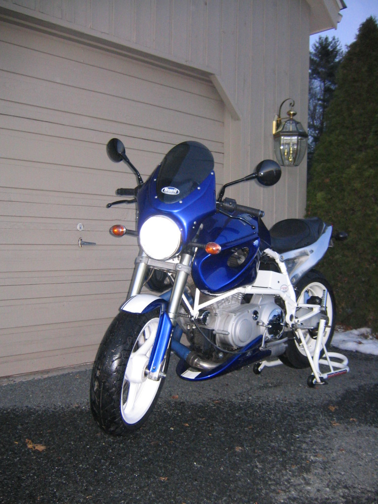 Blue and white Buell motorcycle with fairing parked by a garage, 3/4 front view.