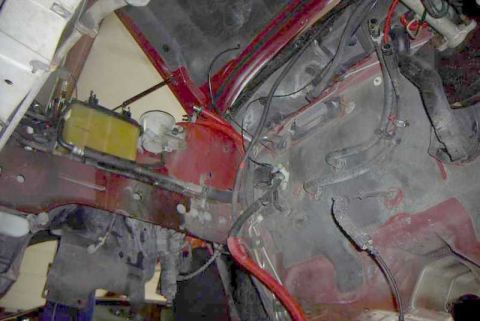 1997 Ford Taurus - Looking down into a stripped engine bay with the engine and subframe removed, exposing the red inner fender aprons, firewall insulation pad…