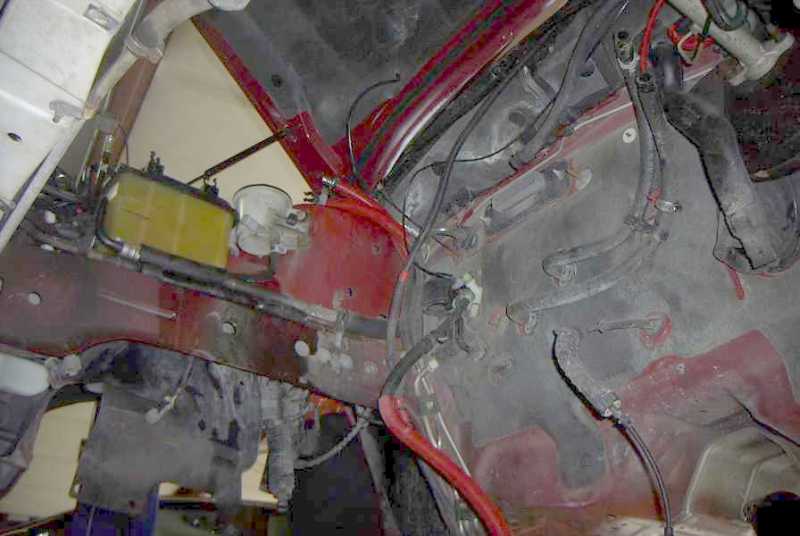 Empty engine bay of red car with bare firewall, inner fenders and hanging wiring harness