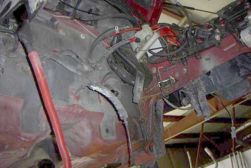 Red vehicle chassis with exposed wiring and hoses in an empty engine bay