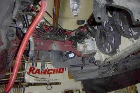 1997 Ford Taurus - Engine bay stripped down to bare firewall and inner fenders, with red-painted structure, an orange flexible intake duct, loose wiring harne…