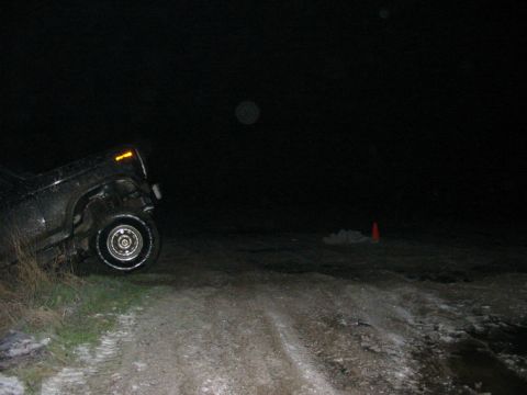 1982 Ford Bronco - A vehicle is stuck in a ditch on a dirt road at night, with a traffic cone visible in the background.