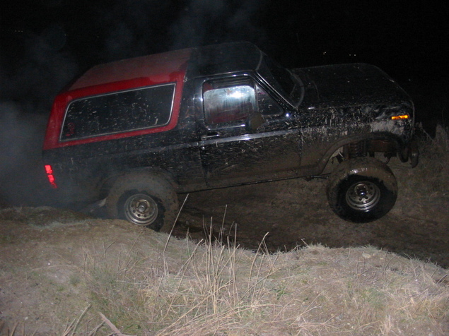 Black and red Ford Bronco with mud on body, driving off-road at night