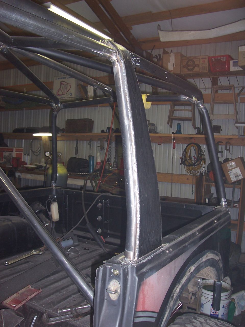 Bare-metal roll cage framework over a truck bed inside a sheet-metal shop