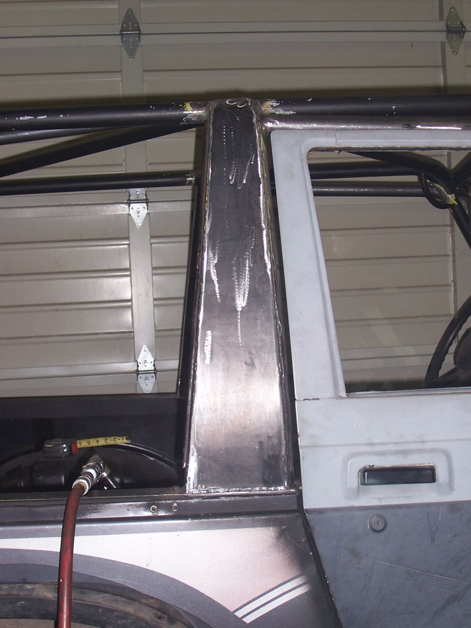 Welded steel B-pillar cage tube tying into door frame, garage door behind