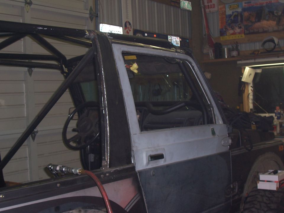 Partially caged truck cab with bare door, steering wheel and dash visible inside a shop