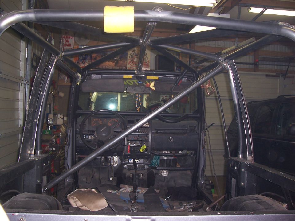 Front view into stripped truck cab through windshield showing full roll cage and dash