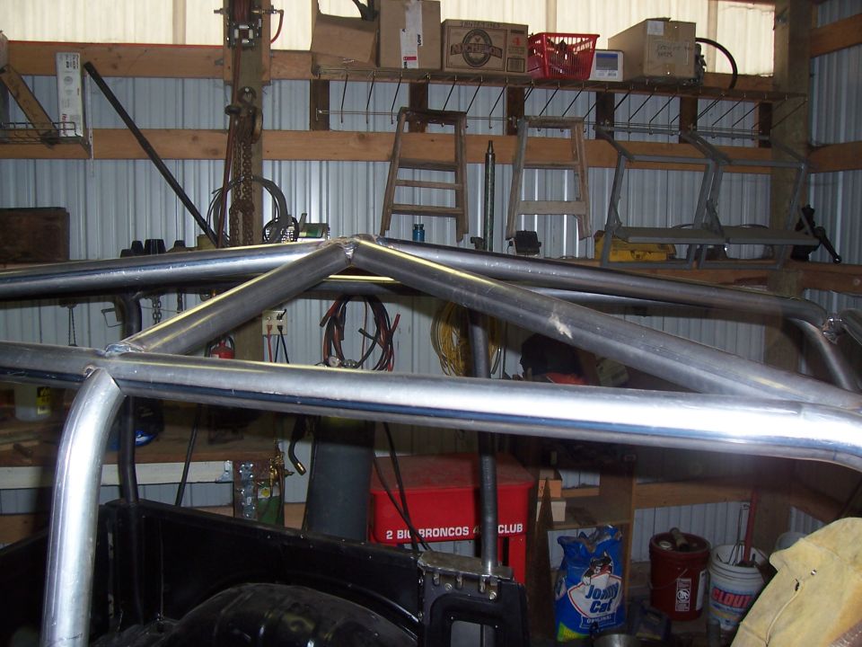 Rear roll cage hoops of a project rig with '2 Big Broncos 4 Wheel Club' sign behind