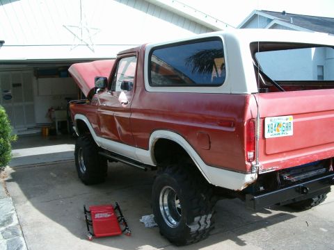 1979 Ford Bronco - This lifted Ford Bronco has its hood up, parked in front of a garage.