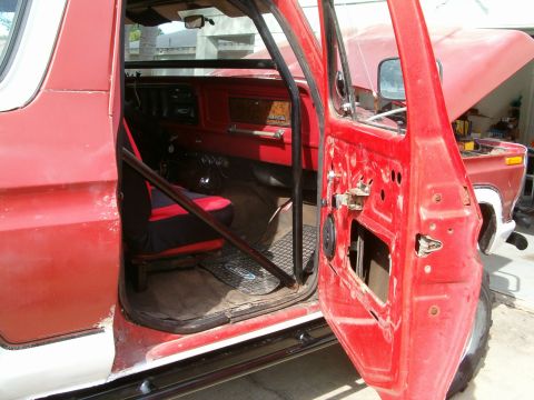 1979 Ford Bronco - Interior view of a red SUV with an open door, revealing a roll cage and engine bay.
