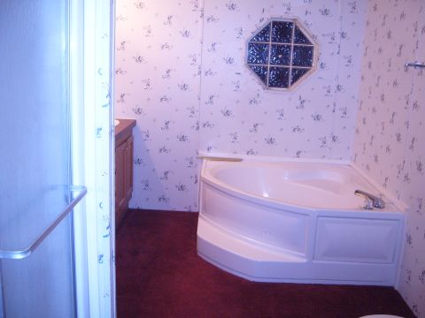1988 Ford Bronco - Interior view of a bathroom a corner bathtub, wooden vanity, and a decorative octagonal window with stained glass.