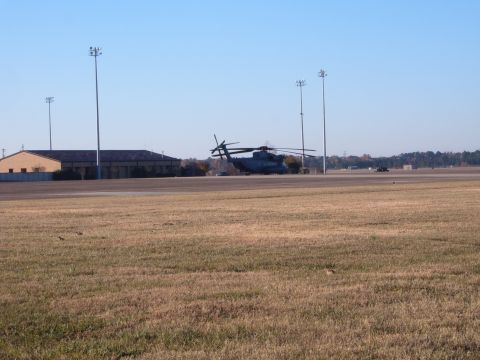 1988 Ford Bronco - Helicopter sits on a grassy airfield next to buildings under a clear blue sky.