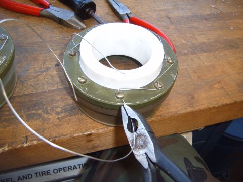 1988 Ford Bronco - Pliers cut wire on a cylindrical part, with tools and another part visible on a workbench.