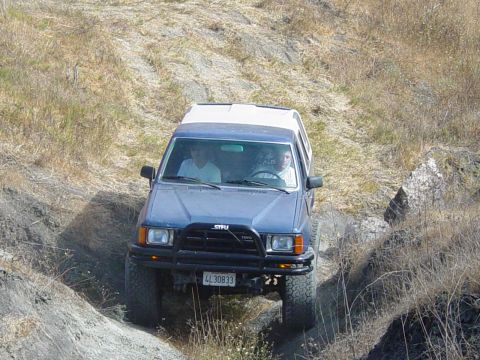 1999 Jeep Grand Cherokee - Blue Toyota 4Runner navigates an off-road trail with two occupants visible inside.