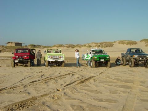 1999 Jeep Grand Cherokee - A group of off-road vehicles are gathered on a sandy beach under a clear blue sky.