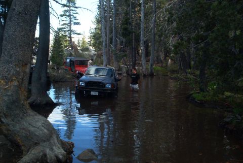 1999 Jeep Grand Cherokee - Two off-road vehicles navigate a water-filled forest path.