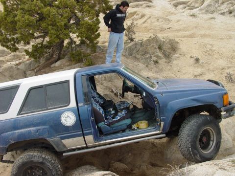 1999 Jeep Grand Cherokee - Off-road pickup truck with a camper shell navigating a rocky trail.