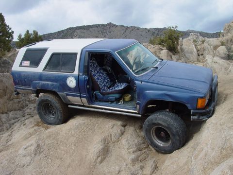 1999 Jeep Grand Cherokee - A blue pickup truck with a white camper shell navigates a rocky, off-road path.
