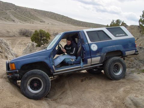 1999 Jeep Grand Cherokee - This modified blue SUV, likely a Toyota 4Runner, navigates rough terrain with its doors open and a white camper shell.