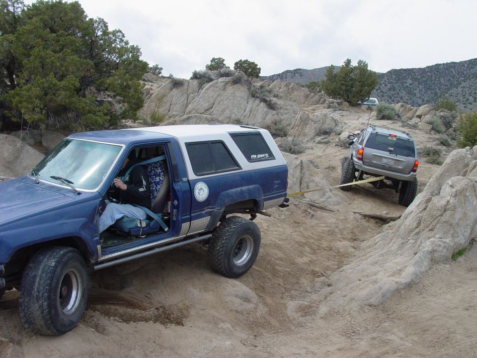 Blue off-road SUV being towed by a silver Jeep Grand Cherokee on a rocky trail