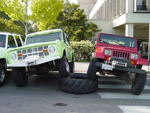 1999 Jeep Grand Cherokee - Two modified off-road vehicles are positioned on tires in a parking lot.