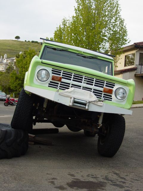 1999 Jeep Grand Cherokee - This lifted 1977 Ford Bronco is tilted, with its front passenger wheel elevated on blocks and a large tire.