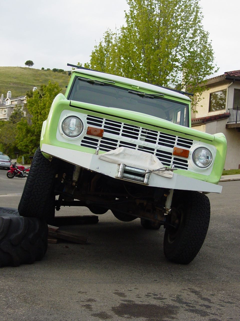 Green and white 1977 Ford Bronco with winch, lifted on one side