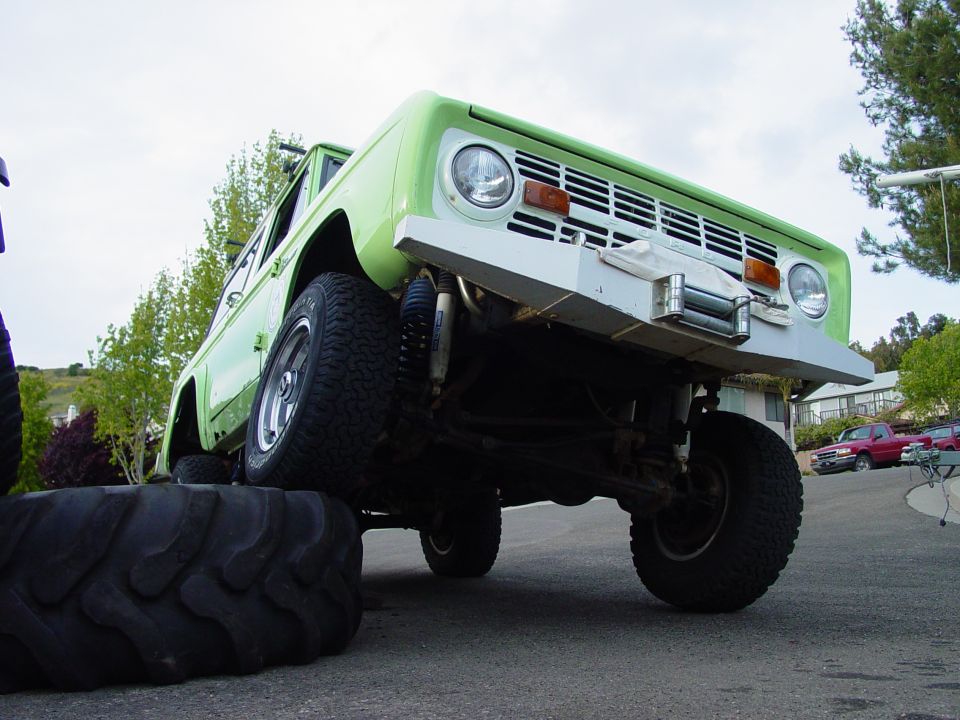 Green 1978 Ford Bronco with custom bumper and winch, front passenger side tire on a large tire