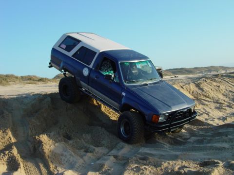 1999 Jeep Grand Cherokee - A blue pickup truck navigates sandy terrain under a clear blue sky.