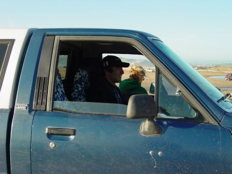 1999 Jeep Grand Cherokee - A blue pickup truck with a white camper shell is parked on a beach with two people inside.