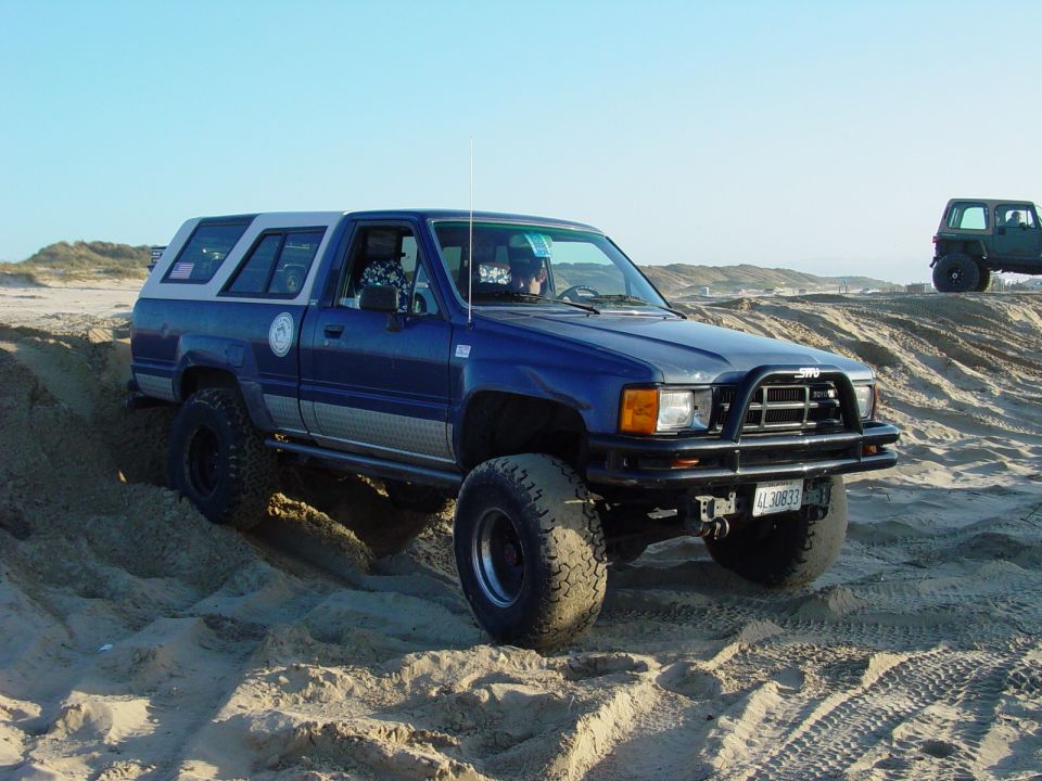 Blue pickup truck with camper shell on sand dunes, front view. License plate LL30833