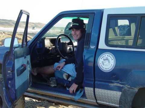 1999 Jeep Grand Cherokee - A man smiles from the driver's seat of a blue Toyota 4x4 truck parked on a sandy surface.