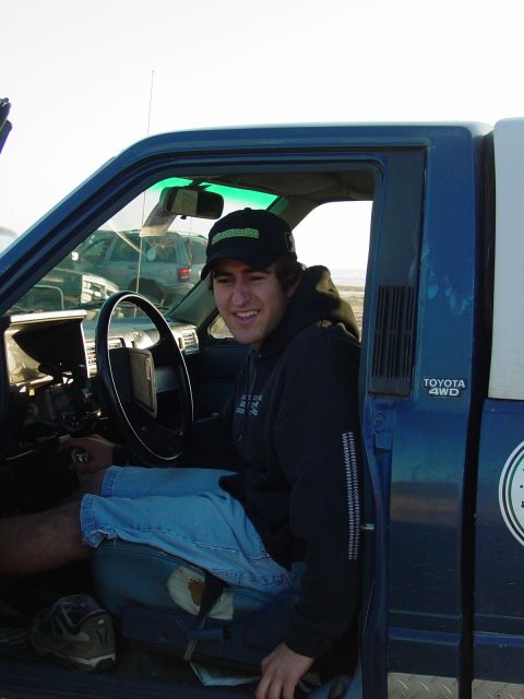 1999 Jeep Grand Cherokee - A man sits in the driver's seat of a blue pickup truck, with another vehicle visible in the background.