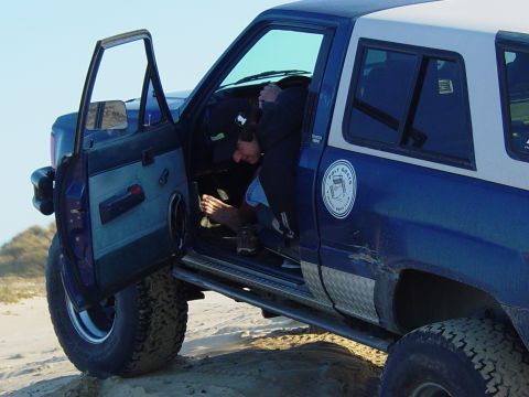 1999 Jeep Grand Cherokee - A person is inside the driver's side of a blue and white SUV, with the door open.