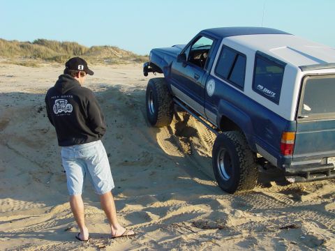 1999 Jeep Grand Cherokee - A man stands near a modified SUV driving on a sandy incline.