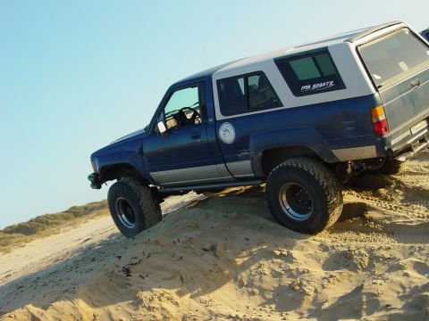 1999 Jeep Grand Cherokee - This SUV is shown off-roading on a sandy terrain under a clear blue sky.