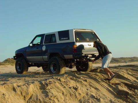 1999 Jeep Grand Cherokee - SUV on a sand dune with a person inspecting the rear tire.